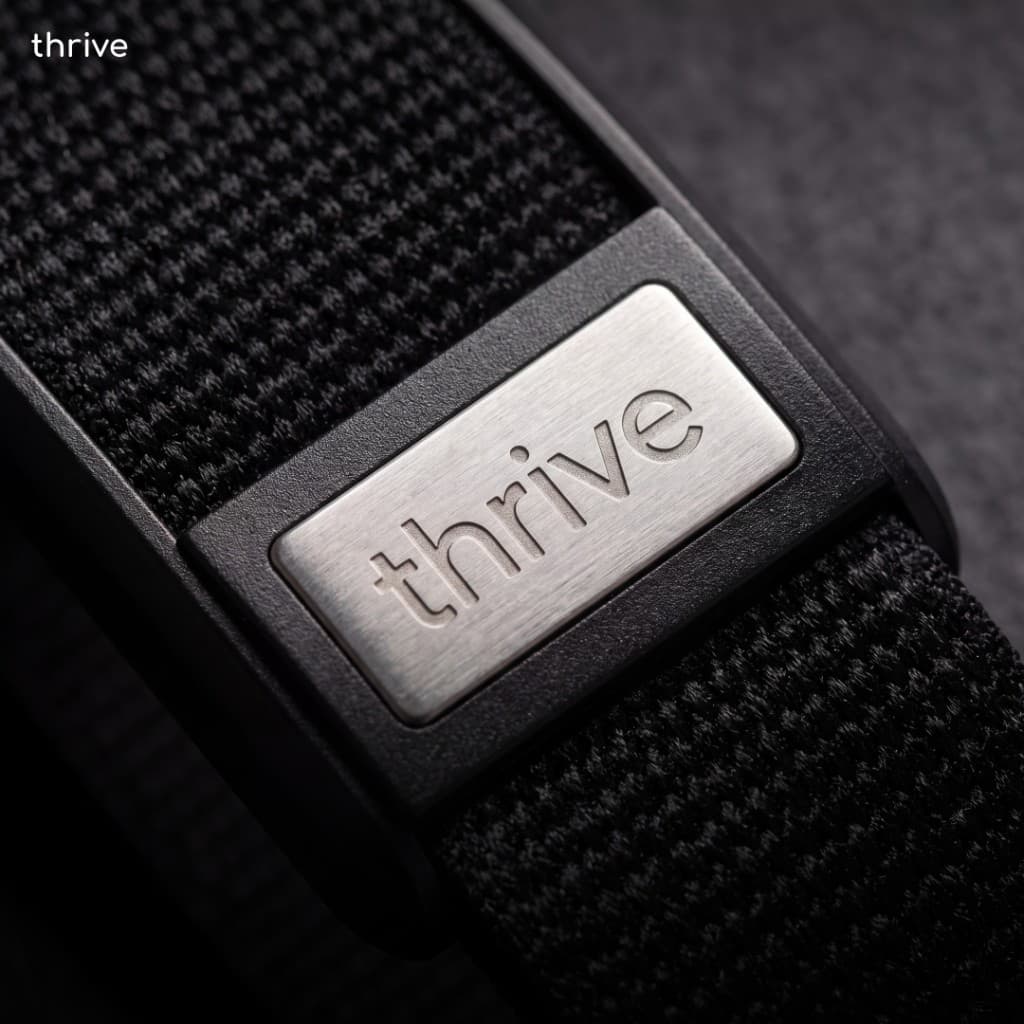 Close-up of the Thrive Band showing the brushed metal clasp with engraved thrive logo and black woven fabric strap.